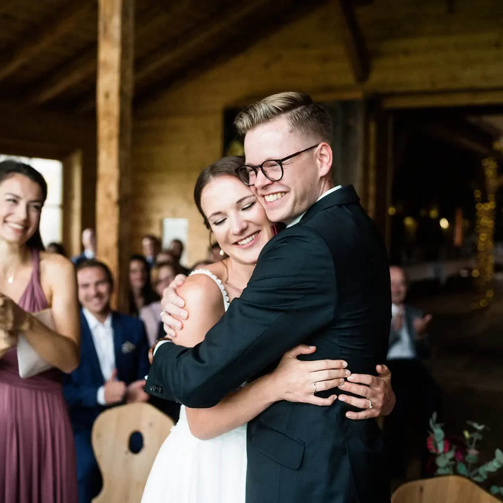 Brautpaar umarmt sich strahlend, umgeben von applaudierenden Gästen bei Hochzeit in den Lenderstuben Balzhausen. Fotografiert vom Hochzeitsfotograf aus Ulm